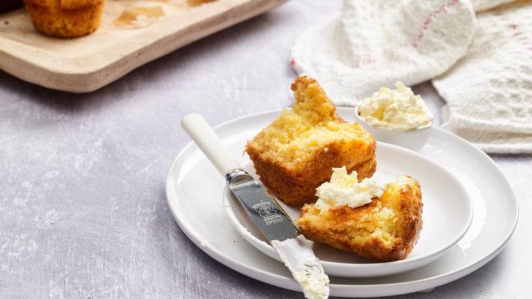 A honey cornbread muffin cut in half with a small amount of whipped honey butter on top